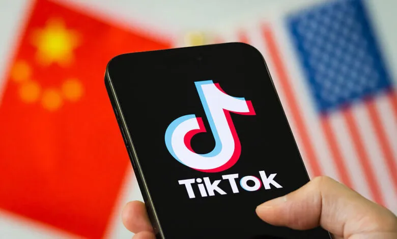 TikTok logo on a smartphone with blurred US and Chinese flags in the background.