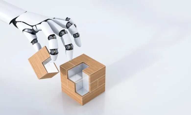 A white robotic arm carefully places a wooden puzzle piece into a cube-shaped structure.