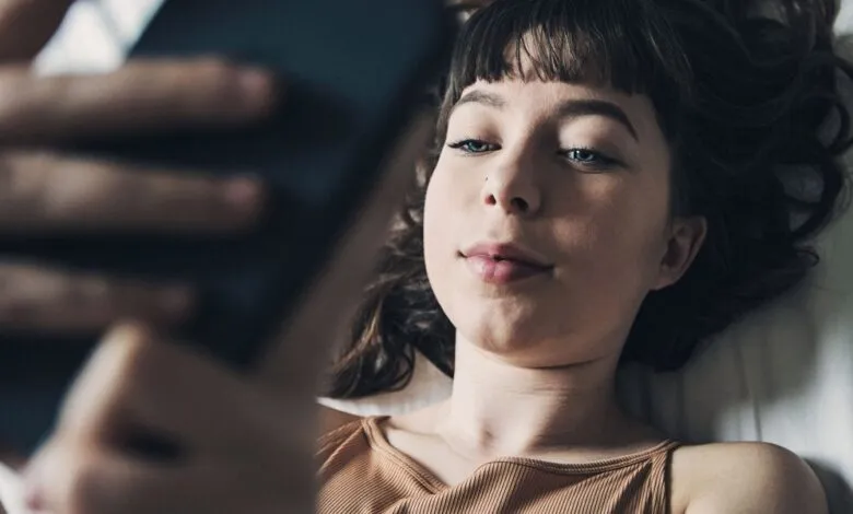 Young woman lies in bed, engrossed in her smartphone.