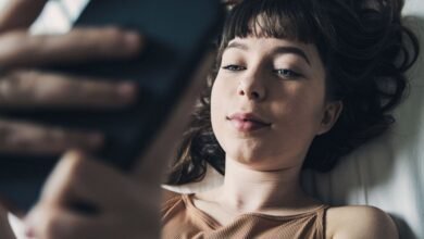 Young woman lies in bed, engrossed in her smartphone.