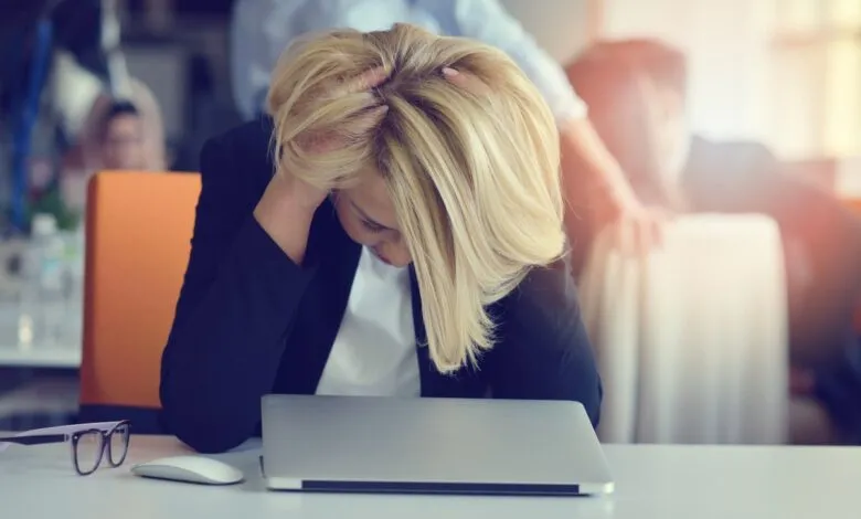 Woman with blonde hair holding her head in despair at a desk with a laptop.