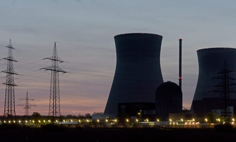 Silhouetted nuclear power plant at dusk, with tall cooling towers and electricity pylons.