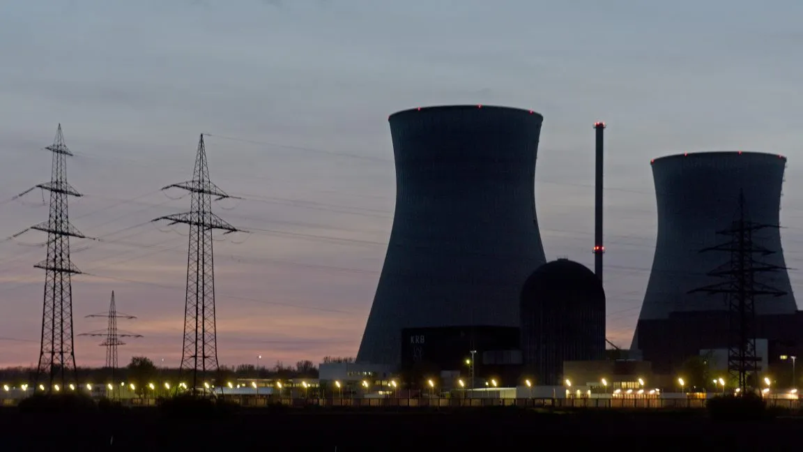 Silhouetted nuclear power plant at dusk, with tall cooling towers and electricity pylons.