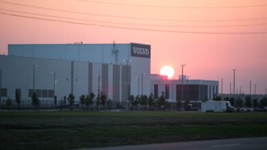 Volvo car factory at sunset. Large white building with Volvo logo, pink sky.