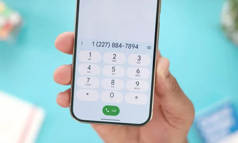 Close-up of a hand holding a smartphone with the dialer app open, displaying a phone number.