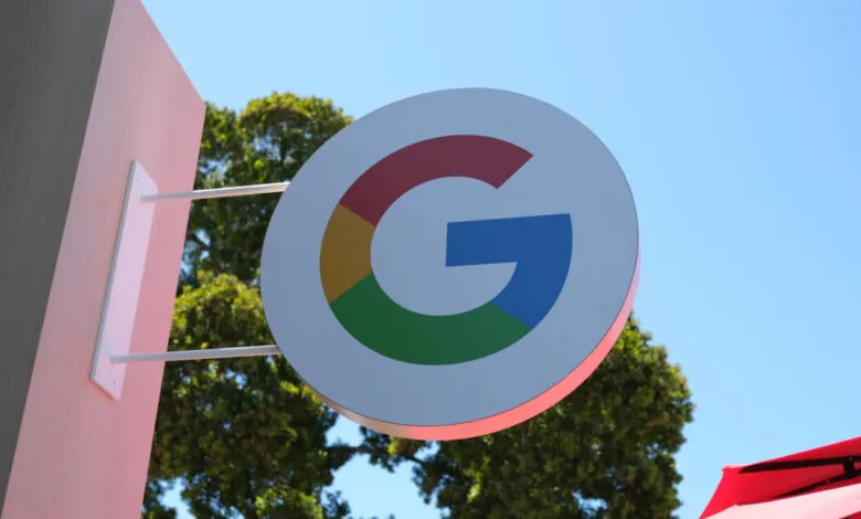Google logo on a round sign, mounted on a pink building against a blue sky.