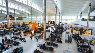 Busy Heathrow Airport terminal with passengers waiting at gates, shops, and restaurants visible.