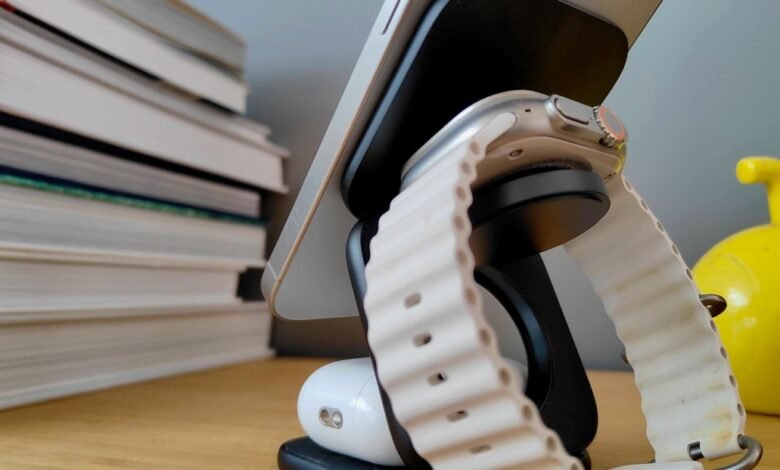 Apple iPhone and Apple Watch on a charging stand, next to a stack of books.