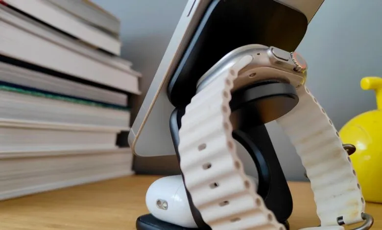 Apple iPhone and Apple Watch on a charging stand, next to a stack of books.