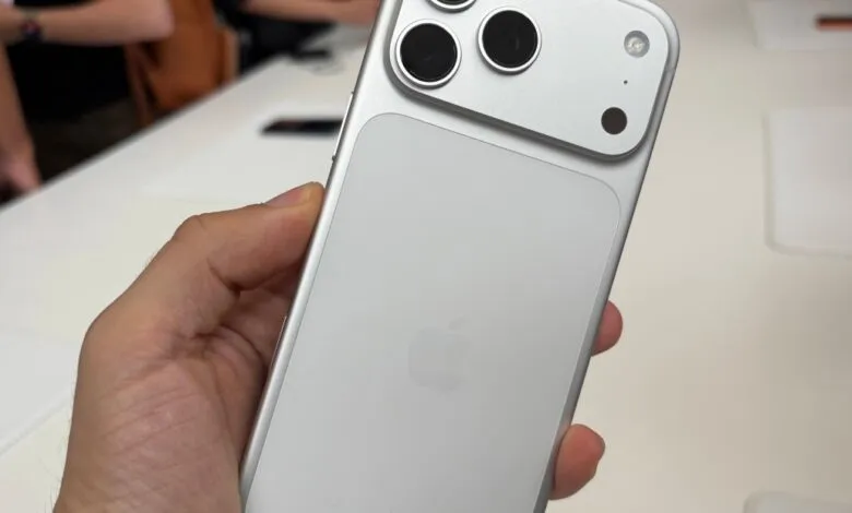Close-up of a person holding a silver iPhone with a prominent camera array on the back.