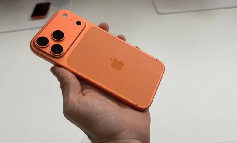 Close-up of a person holding a vibrant orange iPhone with a triple-lens camera.