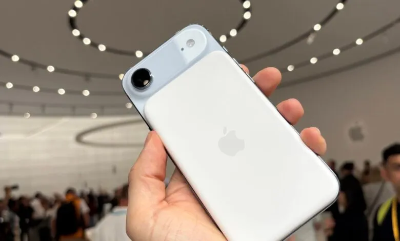 Close-up of a person holding a white iPhone with a prominent camera bump, showcasing the Apple logo on the back.