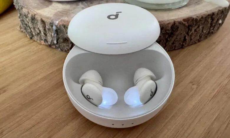 Pair of white Anker Soundcore earbuds charging in their case on a wooden surface.
