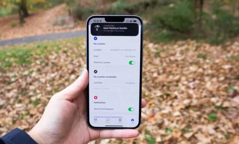Hand holding iPhone displaying Find My location settings, showing satellite connection in progress outdoors.