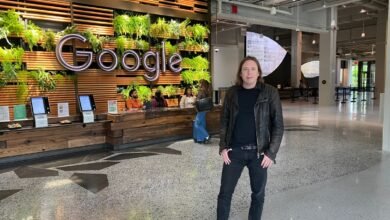 Person standing in Google's modern lobby, featuring a large illuminated Google logo and a living wall.