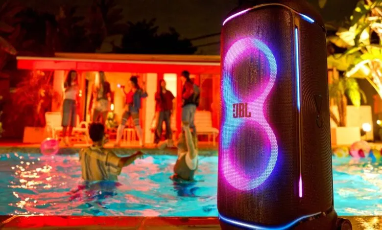 JBL PartyBox 720 portable speaker with vibrant LED lights at a pool party.