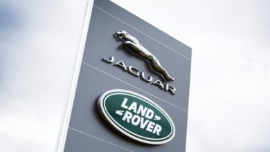 Jaguar and Land Rover logos on a gray sign against a cloudy sky.