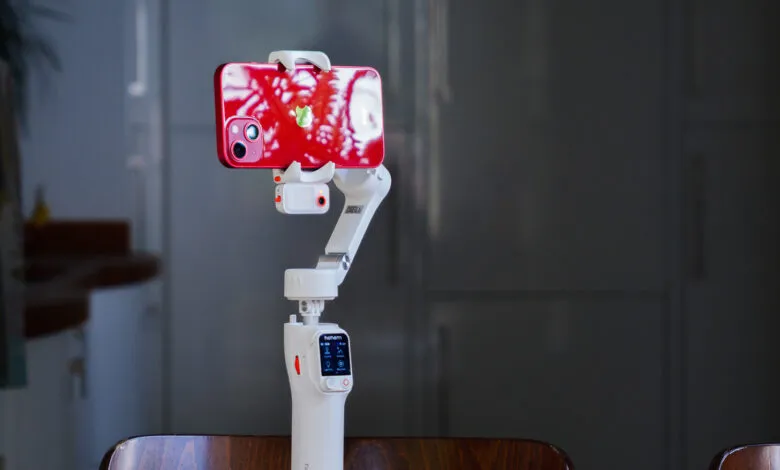 Red iPhone on a white smartphone gimbal, ready for filming.