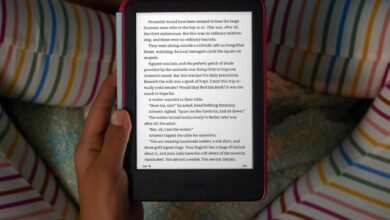 Person holding a pink Kindle e-reader with text displayed.