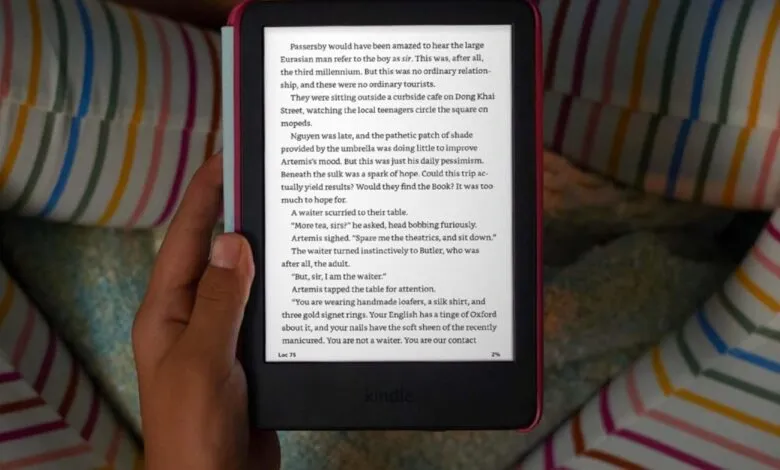 Person holding a pink Kindle e-reader with text displayed.