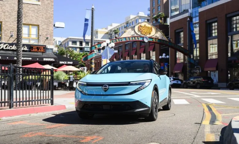 A light blue Nissan Ariya electric SUV drives through a city street.