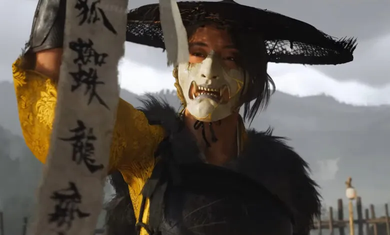 A woman in a yellow and black outfit, wearing a oni mask and wide-brimmed hat, holds a scroll with Asian characters.