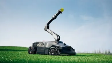 Robotic lawn mower with articulated arm holding a yellow ball on a green lawn under a blue sky.