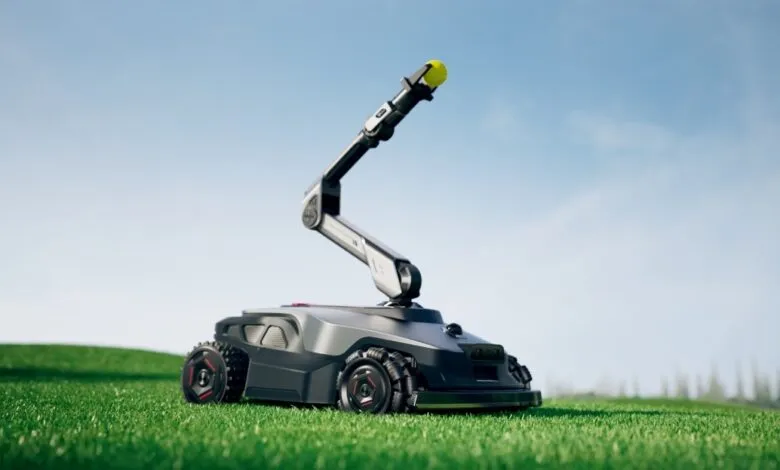 Robotic lawn mower with articulated arm holding a yellow ball on a green lawn under a blue sky.
