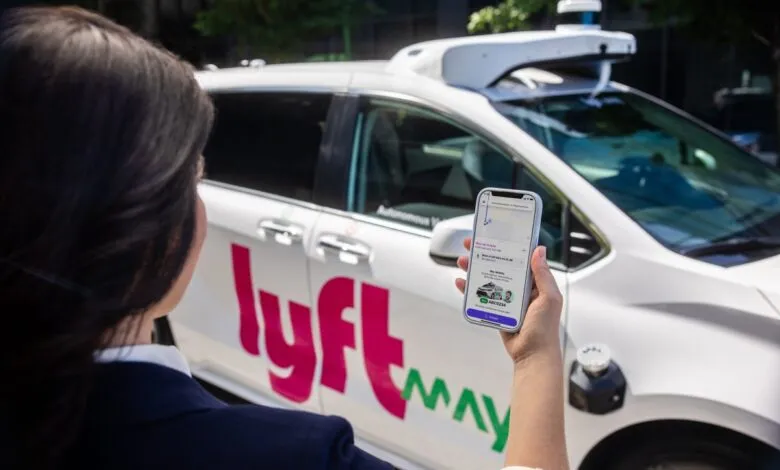 Person uses Lyft app to hail a self-driving car. The Lyft logo is visible on the car.