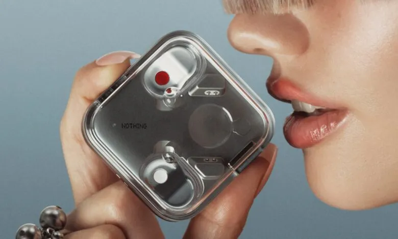 Close-up of a person holding Nothing Ear (3) earbuds in a transparent case. The case shows internal components.