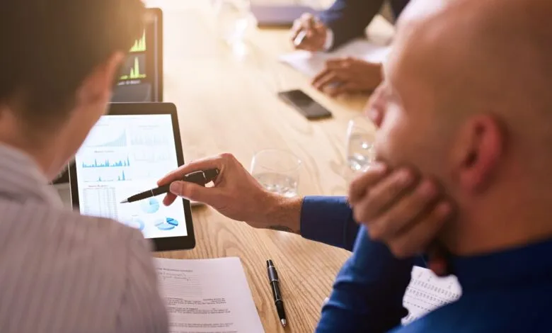Business colleagues review financial data on a tablet during a meeting.