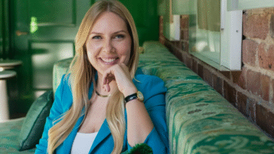 Smiling woman with blonde hair in teal blazer sits on a green patterned couch.