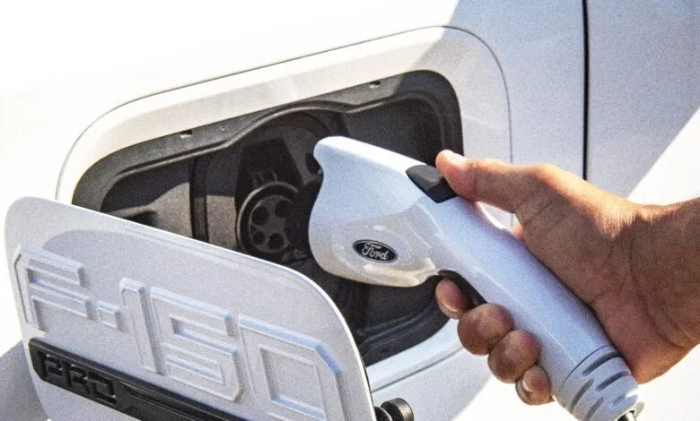 Close-up of a hand plugging a white Ford charging cable into a white F-150 Lightning electric truck.