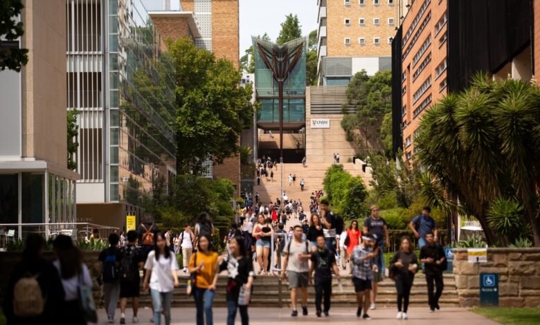 Students walk along a paved pathway at UNSW Sydney's Kensington campus, with modern buildings and lush greenery in the background.