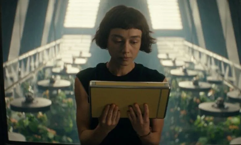 Woman with short hair reads a yellow tablet in a futuristic greenhouse.
