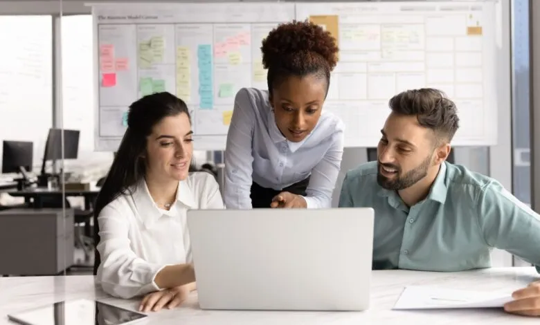 Three colleagues collaborate on a laptop, reviewing project data together in a modern office.