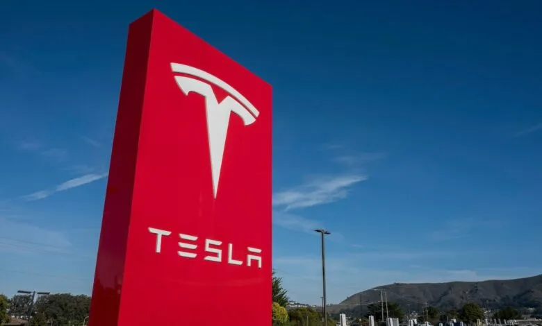 Large red Tesla sign with white logo against a clear blue sky.