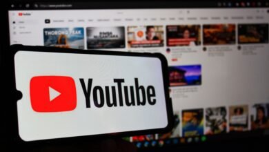 YouTube logo displayed on a smartphone with a blurred YouTube homepage in the background.