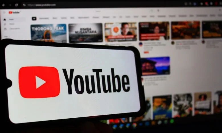 YouTube logo displayed on a smartphone with a blurred YouTube homepage in the background.