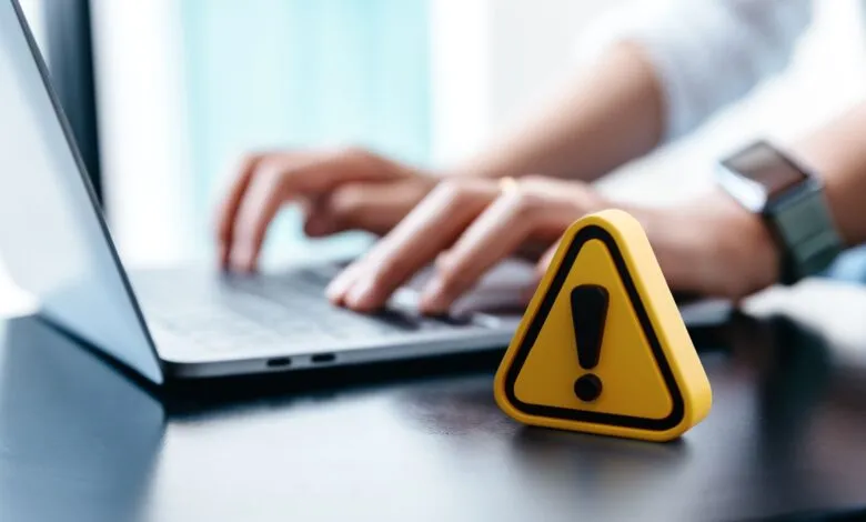 Close-up of hands typing on a laptop with a yellow warning triangle in the foreground.