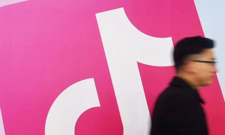 TikTok logo on a pink wall with a person walking by.