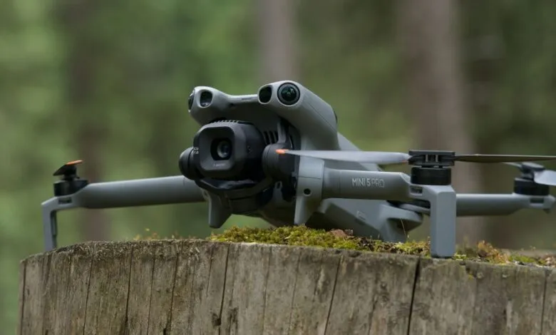 A gray DJI Mini 5 Pro drone rests on a moss-covered wooden stump in a forest.