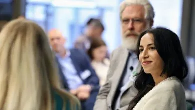 Noor Siddiqui, a scientist, smiles subtly during a conference, with George Church in the background.