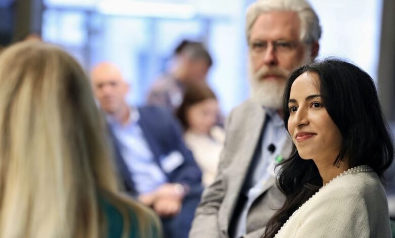 Noor Siddiqui, a scientist, smiles subtly during a conference, with George Church in the background.