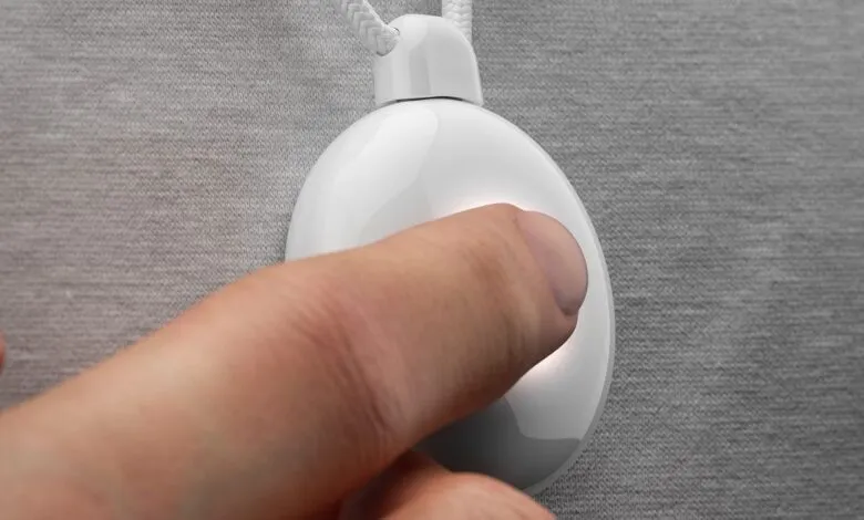 Close-up of a finger pressing a button on a white oval medical alert pendant.