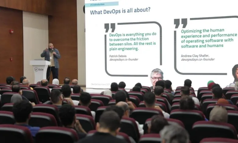Speaker presenting on DevOps at a conference with audience in foreground.