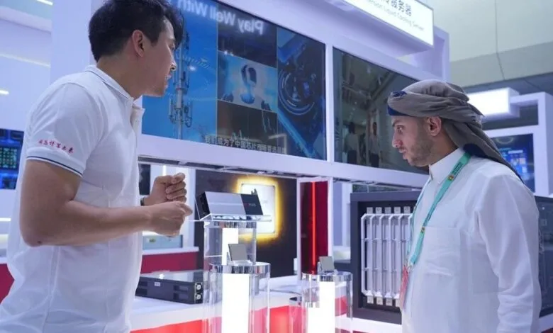 Two men in business attire discuss technology at a trade show booth featuring AI and telecommunications equipment displays.