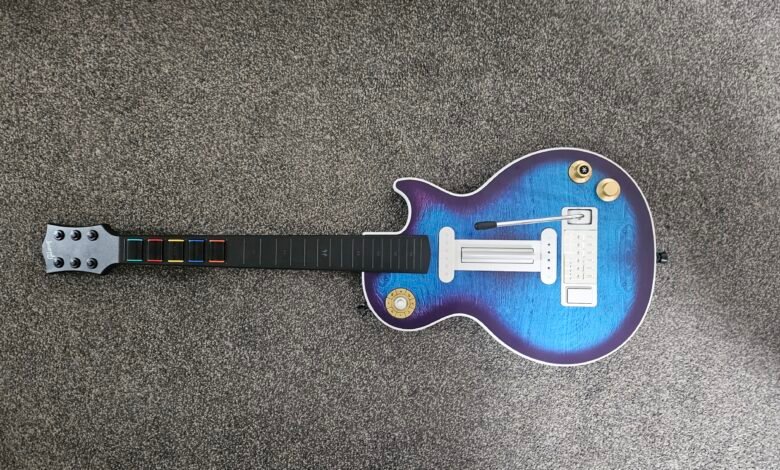 A video game guitar controller with a blue and purple wood grain finish on a grey carpet.