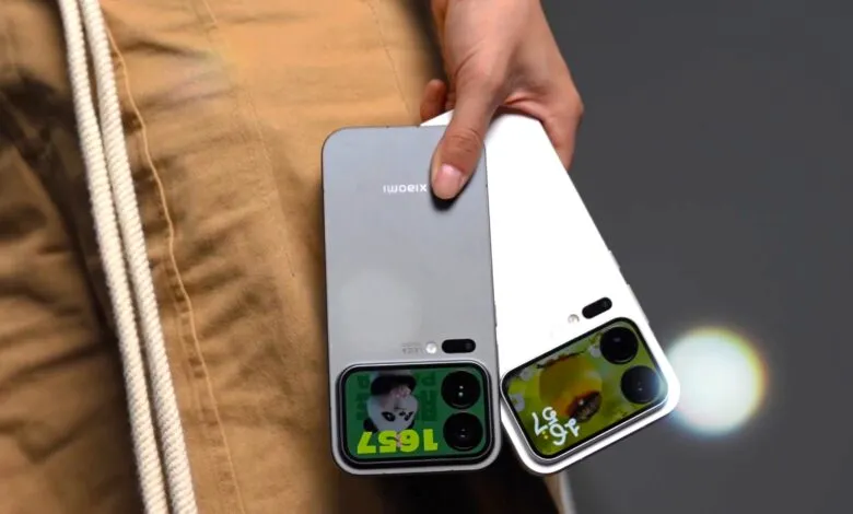 Two smartphones, one silver and one white, held by a person wearing tan pants.