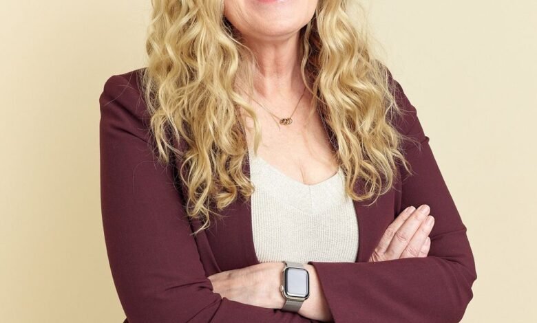Smiling woman with blonde hair, wearing a burgundy blazer and Apple Watch.
